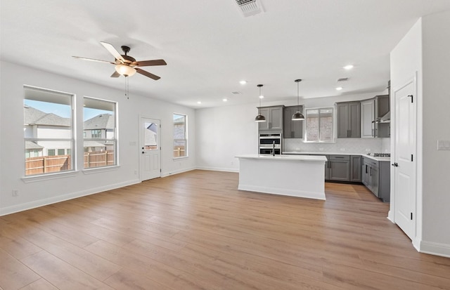 217 Canyoncrest Way, Liberty Hill, TX 78642 - kitchen featuring gray cabinetry, open floor plan, ceiling fan, backsplash, and an island with sink
