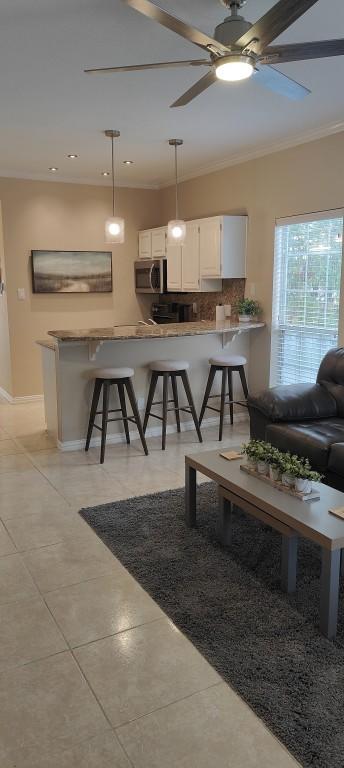 kitchen with kitchen peninsula, decorative backsplash, decorative light fixtures, a kitchen bar, and white cabinetry