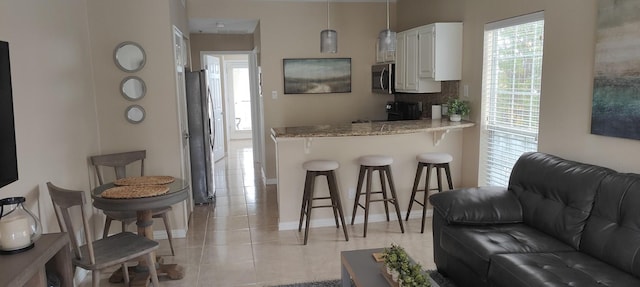 kitchen featuring white cabinets, a breakfast bar area, light tile patterned flooring, light stone counters, and stainless steel appliances