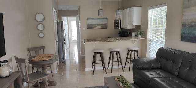 kitchen with white cabinetry, stainless steel appliances, a kitchen breakfast bar, light stone counters, and tasteful backsplash