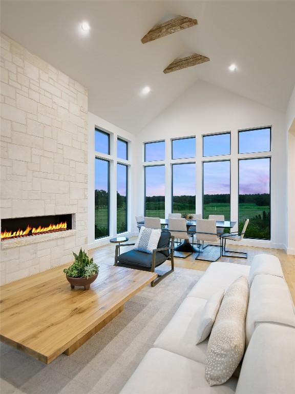 living room featuring light hardwood / wood-style floors, a stone fireplace, and high vaulted ceiling