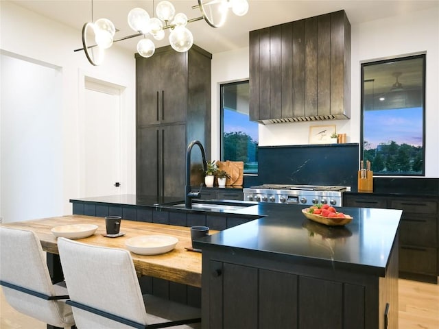 kitchen with pendant lighting, a center island with sink, sink, light wood-type flooring, and dark brown cabinets