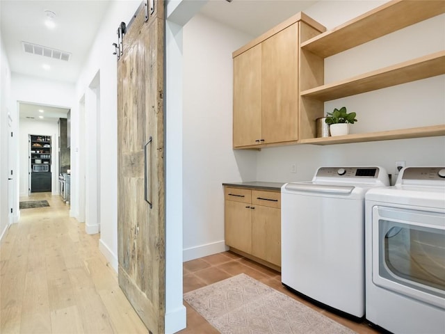 washroom with a barn door, cabinets, light hardwood / wood-style floors, and washing machine and clothes dryer