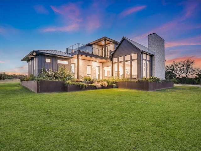 back house at dusk featuring a lawn and a balcony