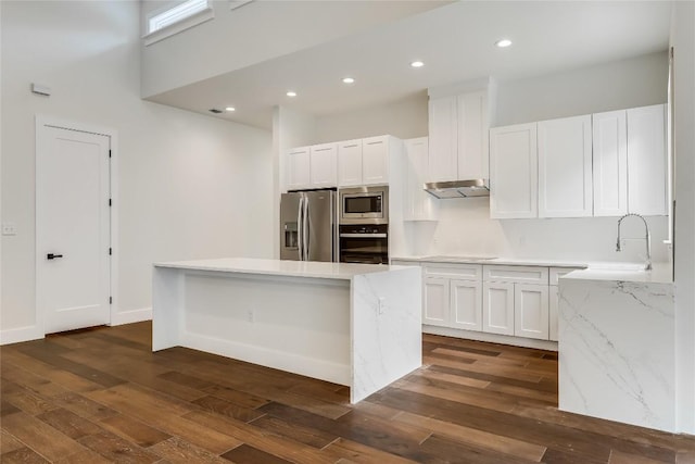 kitchen with a center island, light stone counters, dark hardwood / wood-style floors, white cabinets, and appliances with stainless steel finishes