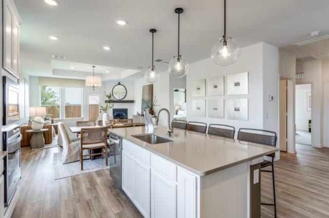 kitchen with white cabinetry, an island with sink, pendant lighting, and light wood-type flooring