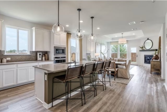 kitchen with a healthy amount of sunlight, stainless steel appliances, an island with sink, pendant lighting, and white cabinets