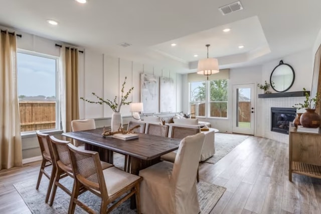 dining area with a fireplace, light wood-type flooring, and a tray ceiling