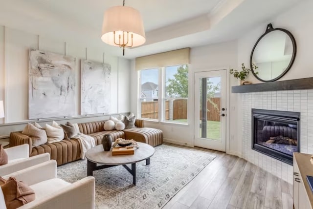 living room with a raised ceiling, a tiled fireplace, and light hardwood / wood-style flooring