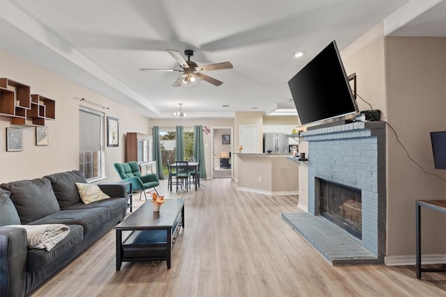 living room with a fireplace, light wood-type flooring, and ceiling fan