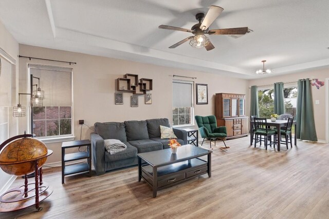 living room featuring a raised ceiling, ceiling fan with notable chandelier, and hardwood / wood-style flooring