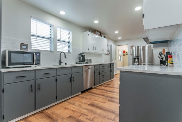 kitchen with appliances with stainless steel finishes, tasteful backsplash, gray cabinetry, sink, and light hardwood / wood-style flooring