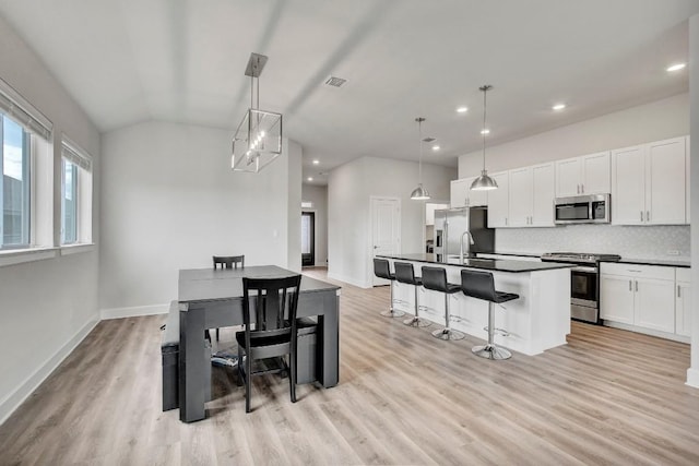 kitchen with pendant lighting, white cabinets, stainless steel appliances, and an island with sink