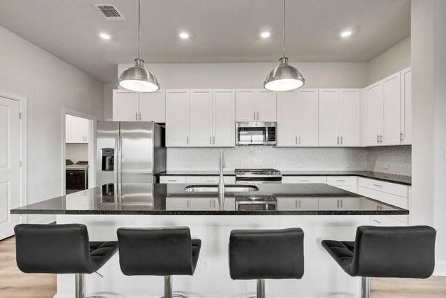 100 Patrick Herndon Dr, Bastrop, TX 78602 - kitchen with appliances with stainless steel finishes, decorative backsplash, white cabinets, a kitchen breakfast bar, and a center island with sink