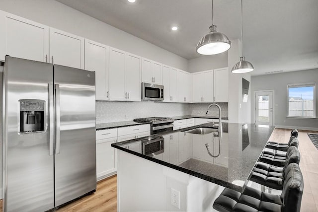 kitchen featuring appliances with stainless steel finishes, dark stone counters, sink, pendant lighting, and light hardwood / wood-style floors