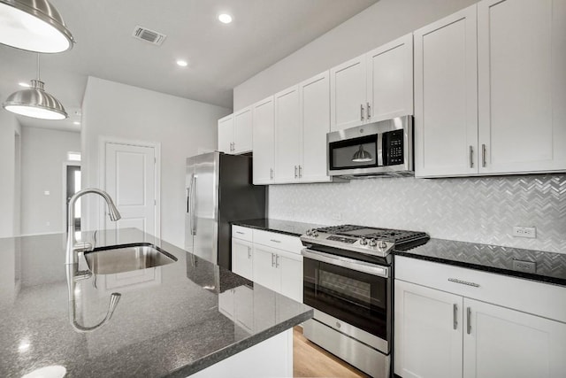 kitchen with stainless steel appliances, white cabinetry, dark stone countertops, and sink