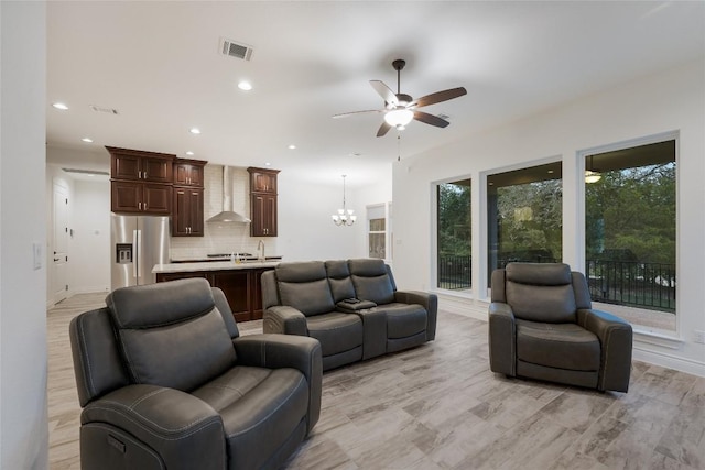 living room featuring ceiling fan with notable chandelier and light wood-type flooring