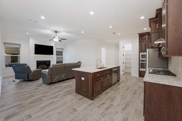 kitchen with a kitchen island with sink, light hardwood / wood-style flooring, ceiling fan, dark brown cabinets, and stainless steel appliances