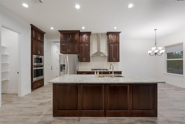 kitchen featuring a center island with sink, sink, wall chimney exhaust hood, stainless steel appliances, and a chandelier