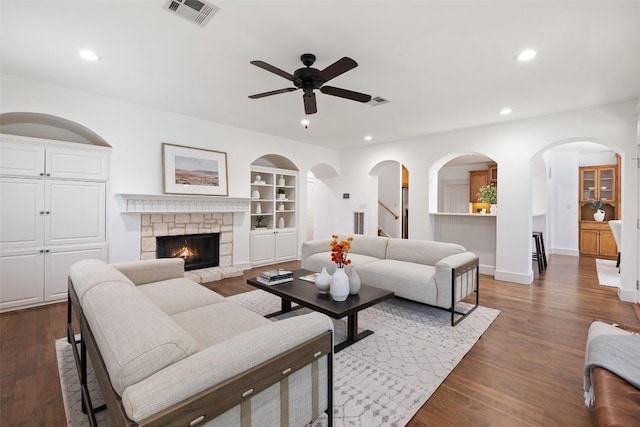 living room with ceiling fan, a fireplace, dark wood-type flooring, and built in features