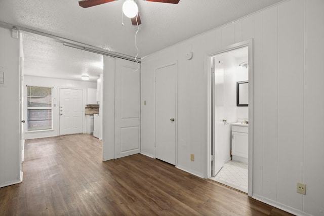 unfurnished bedroom with a textured ceiling, ceiling fan, dark wood-type flooring, and connected bathroom