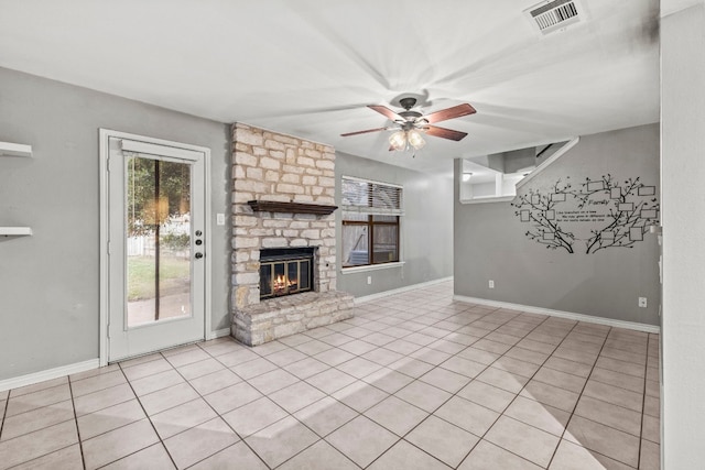 unfurnished living room featuring ceiling fan, a stone fireplace, and light tile patterned floors