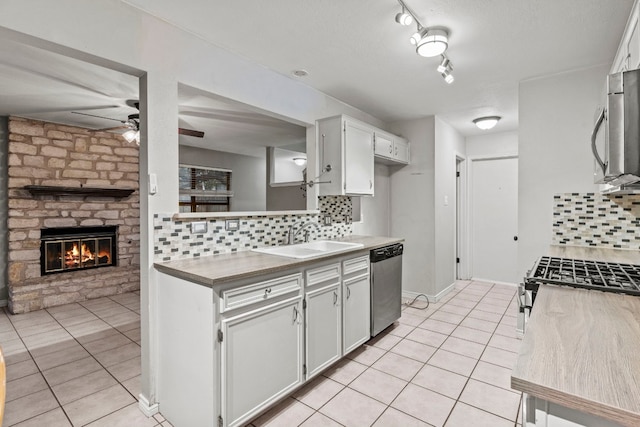 kitchen featuring a stone fireplace, sink, tasteful backsplash, white cabinetry, and stainless steel appliances