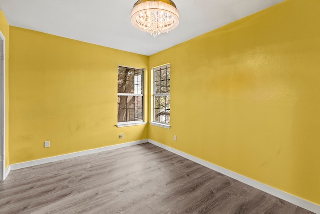 spare room with wood-type flooring and an inviting chandelier