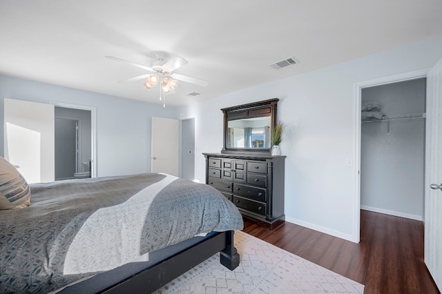 bedroom with a walk in closet, a closet, dark hardwood / wood-style floors, and ceiling fan