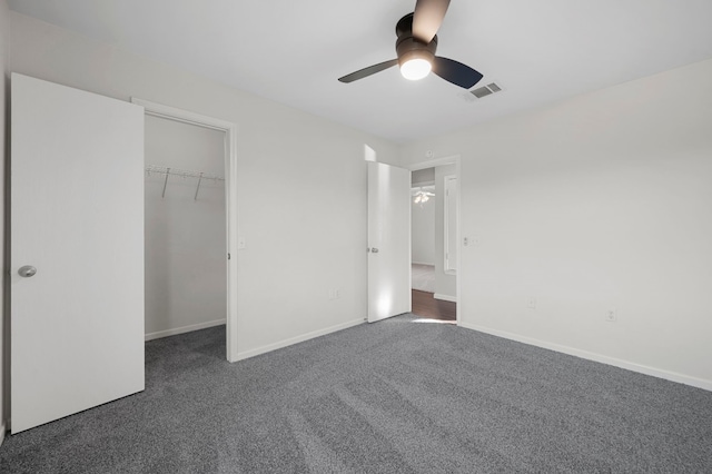 unfurnished bedroom featuring dark carpet, a closet, a spacious closet, and ceiling fan