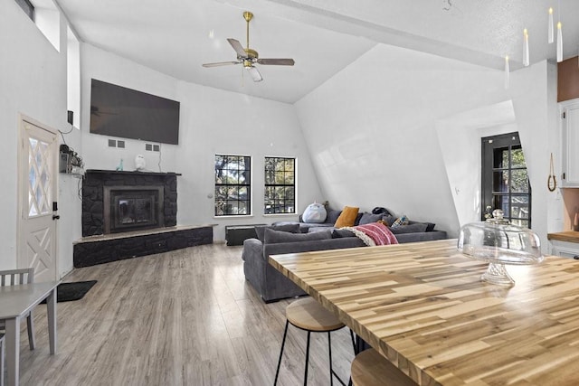 dining space featuring ceiling fan, light hardwood / wood-style floors, a stone fireplace, and high vaulted ceiling