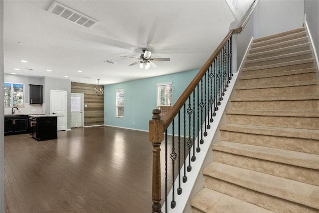 stairs featuring hardwood / wood-style floors, a healthy amount of sunlight, ceiling fan with notable chandelier, and sink