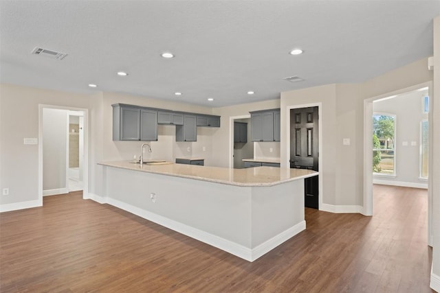 kitchen with gray cabinets, light stone counters, dark wood-type flooring, and sink