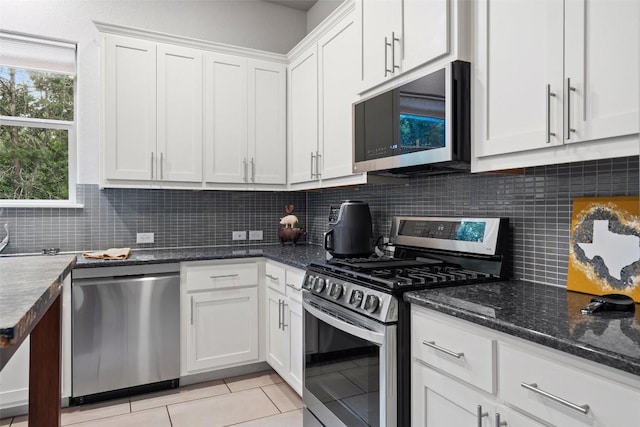 kitchen featuring light tile patterned floors, white cabinets, appliances with stainless steel finishes, dark stone countertops, and backsplash