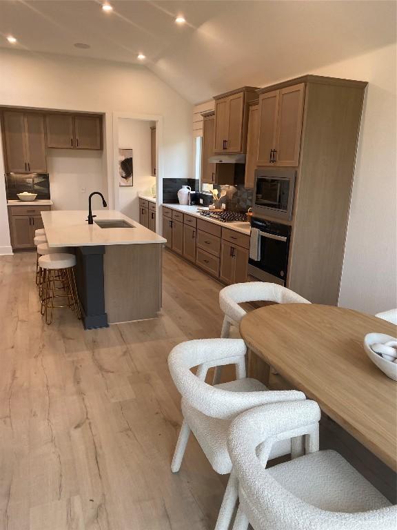 kitchen with lofted ceiling, a kitchen island with sink, sink, light hardwood / wood-style flooring, and stainless steel appliances