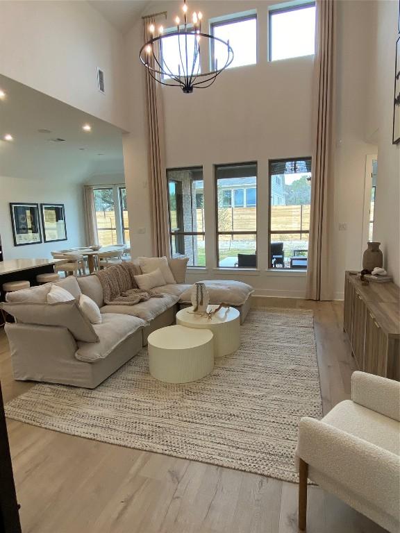 living room featuring a notable chandelier, light wood-type flooring, and a high ceiling