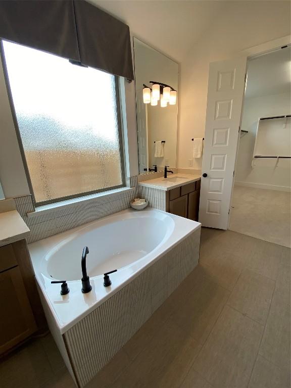 bathroom with vanity, tiled tub, and vaulted ceiling