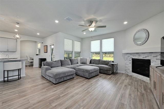 living room featuring ceiling fan, sink, a fireplace, and light wood-type flooring