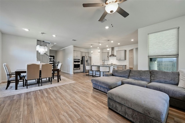 living room featuring sink, ceiling fan with notable chandelier, and light hardwood / wood-style flooring