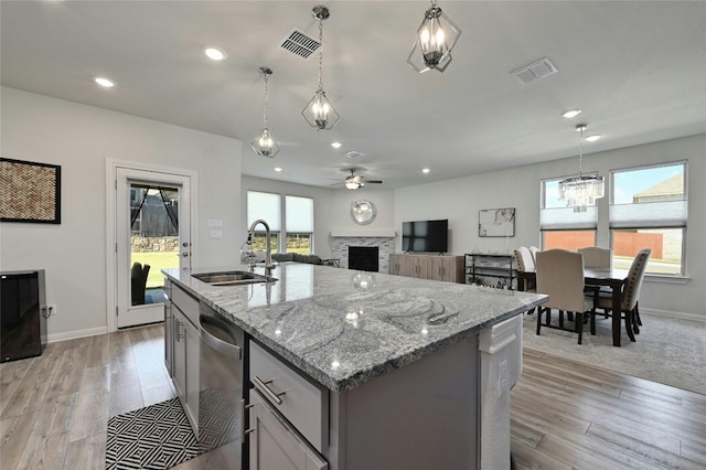 kitchen featuring decorative light fixtures, dishwasher, an island with sink, sink, and light hardwood / wood-style floors