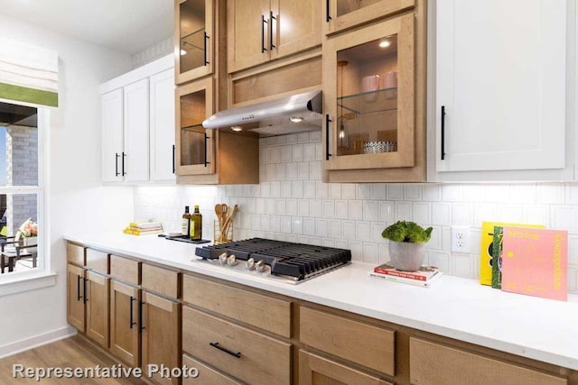 kitchen with light wood-type flooring, backsplash, ventilation hood, stainless steel gas cooktop, and white cabinetry