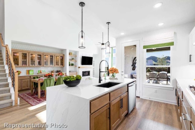 kitchen with sink, decorative light fixtures, light hardwood / wood-style flooring, dishwasher, and an island with sink