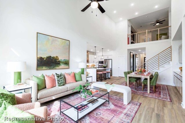 living room featuring ceiling fan, a high ceiling, and light hardwood / wood-style flooring