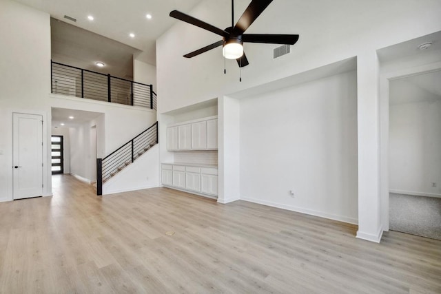 596 Biscayne Bay Bnd, Kyle, TX 78640 - unfurnished living room with a high ceiling, light wood finished floors, a ceiling fan, baseboards, and stairs