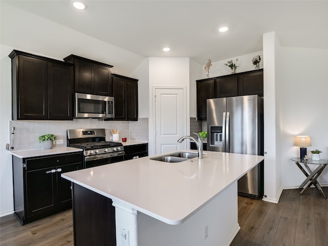 kitchen featuring sink, an island with sink, hardwood / wood-style flooring, stainless steel appliances, and decorative backsplash