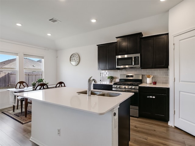 kitchen featuring decorative backsplash, stainless steel appliances, sink, a center island with sink, and dark hardwood / wood-style floors