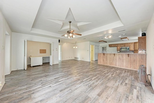 unfurnished living room featuring light hardwood / wood-style flooring, a raised ceiling, and ceiling fan