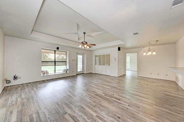 unfurnished living room featuring a raised ceiling, light hardwood / wood-style floors, and ceiling fan with notable chandelier