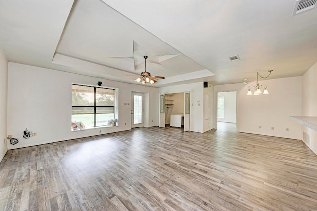 unfurnished living room with ceiling fan with notable chandelier, light hardwood / wood-style floors, and a raised ceiling