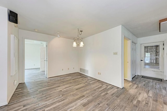 spare room with an inviting chandelier and hardwood / wood-style flooring